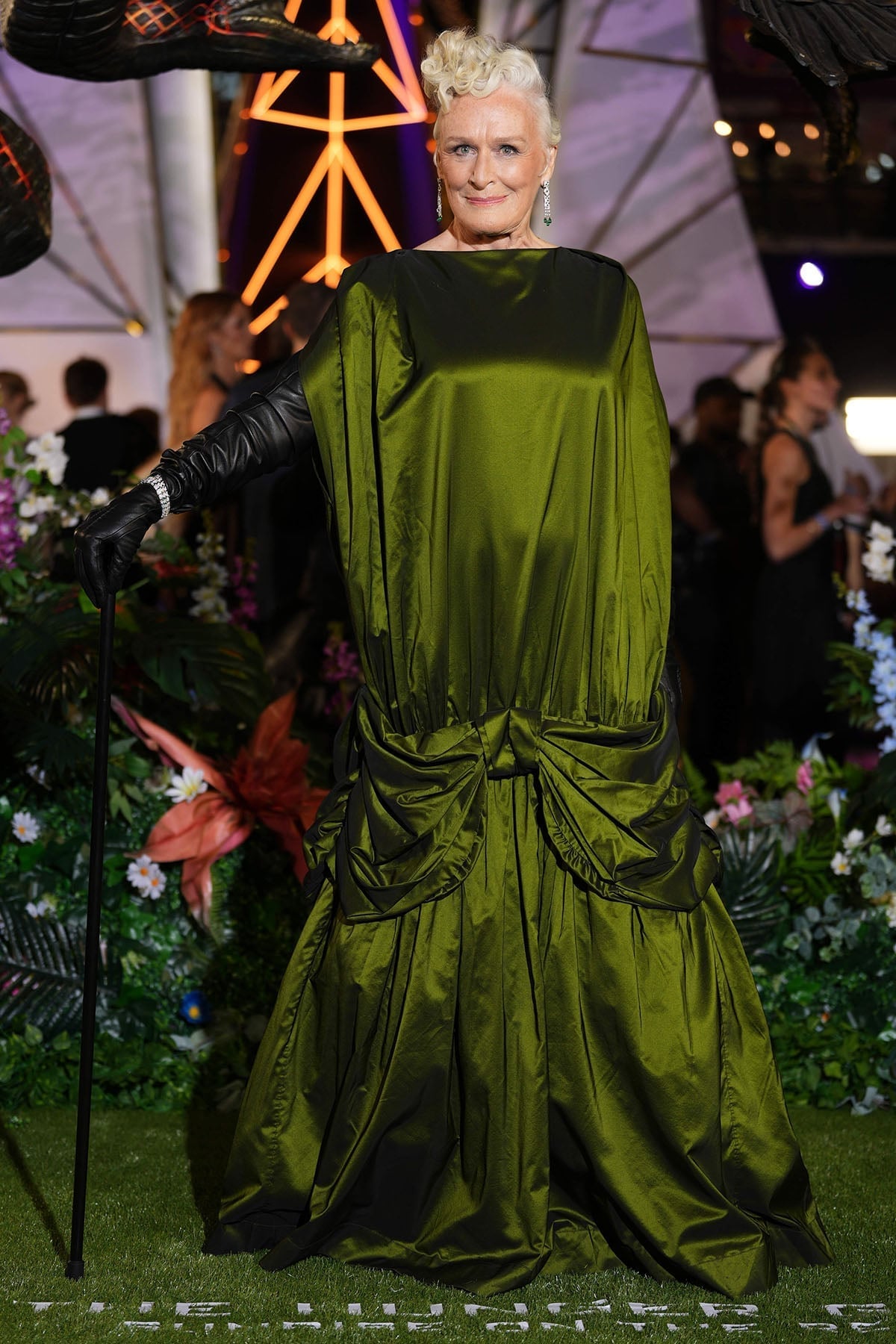 Гленн Клоуз в объёмном зелёном платье Simone Rocha с бантами, в длинных чёрных перчатках и с тростью на лондонской премьере «Голодных игр: Рассвет жатвы», 28 октября 2026