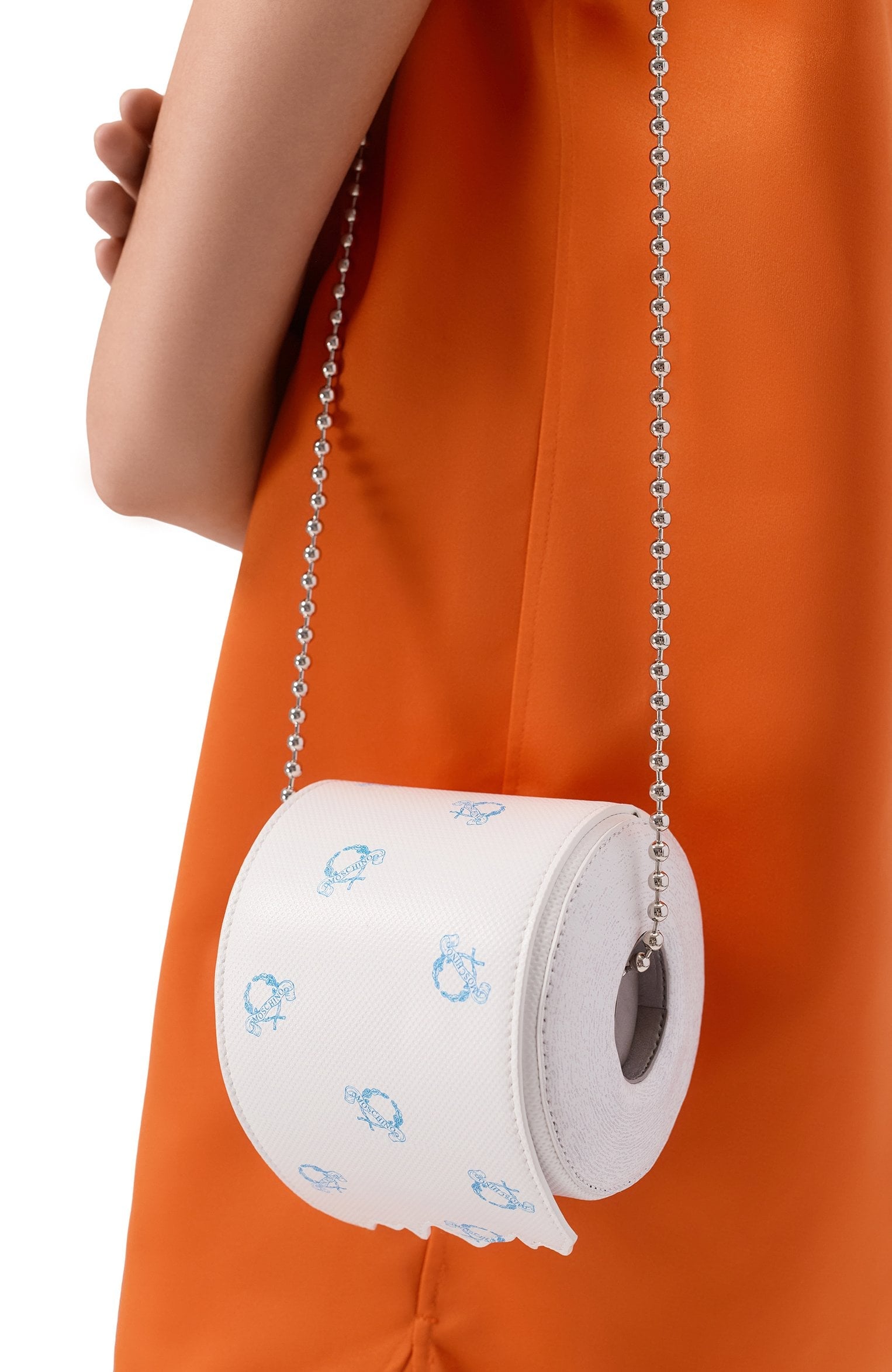 Белая сумка Moschino в виде рулона туалетной бумаги на цепочке из серебристых бусин, на плече модели в оранжевом платье